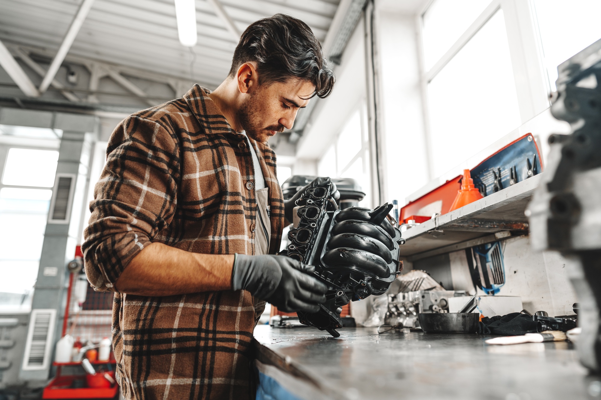 Young man mechanic repairing car parts on worktable in car service shop